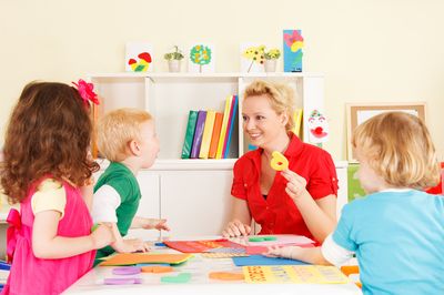 Drei Kinder werden von einer Person betreut. Die Betreuungskraft hält eine Zahl in einer Hand. 